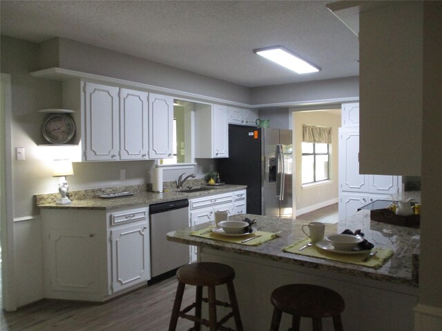 kitchen with a kitchen bar, wood finished floors, white cabinetry, and stainless steel appliances