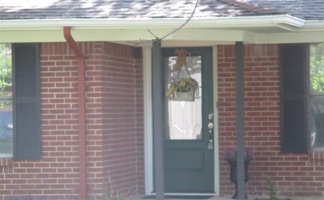 property entrance featuring a shingled roof and brick siding