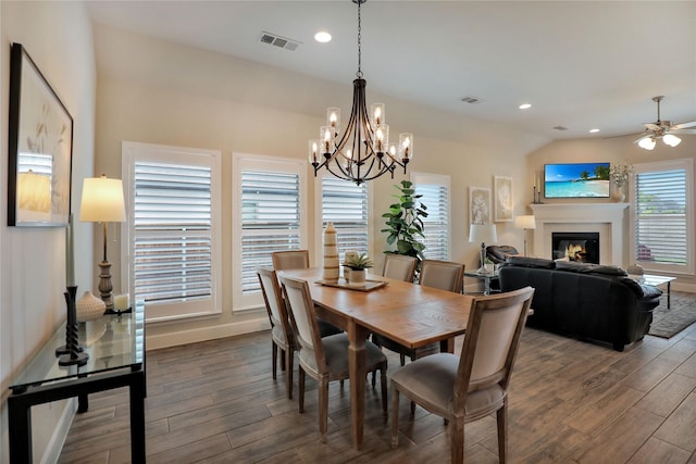 dining space with visible vents, ceiling fan with notable chandelier, dark wood-style flooring, and a glass covered fireplace