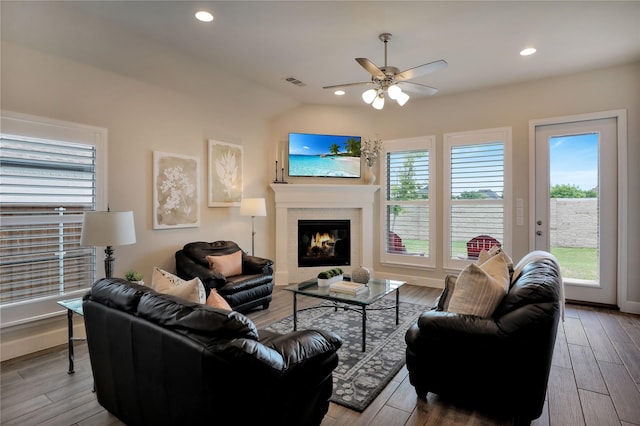living room with a ceiling fan, visible vents, a wealth of natural light, and a glass covered fireplace