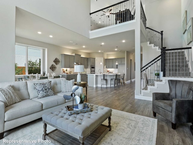 living area featuring stairway, a towering ceiling, dark wood-type flooring, and recessed lighting