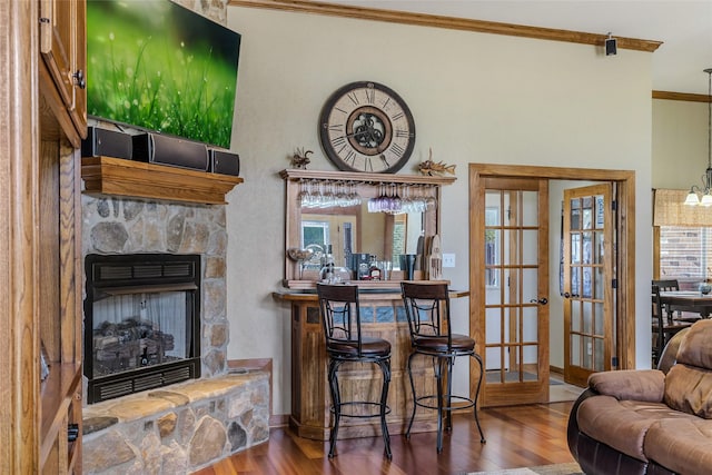 bar with wood finished floors, a stone fireplace, french doors, crown molding, and baseboards
