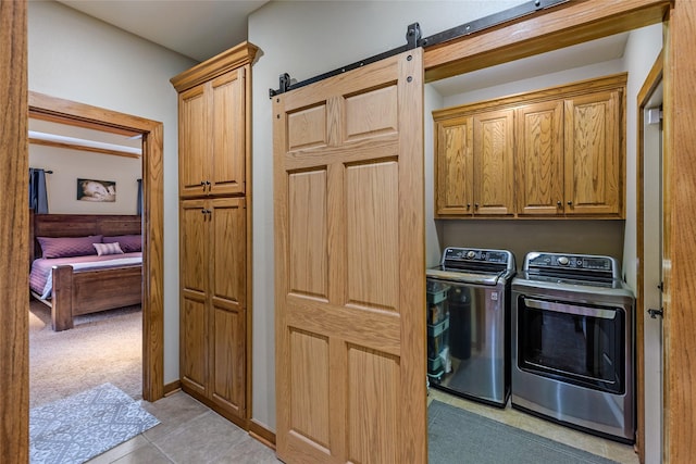 washroom with a barn door, washing machine and clothes dryer, cabinet space, and light tile patterned floors