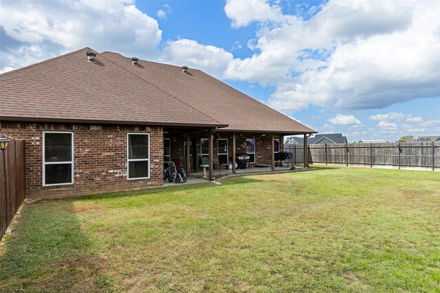back of house featuring a fenced backyard, brick siding, a shingled roof, a yard, and a patio
