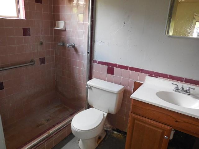 bathroom with a shower stall, toilet, vanity, tile walls, and wainscoting