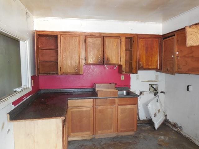 kitchen featuring open shelves, brown cabinetry, unfinished concrete floors, and dark countertops