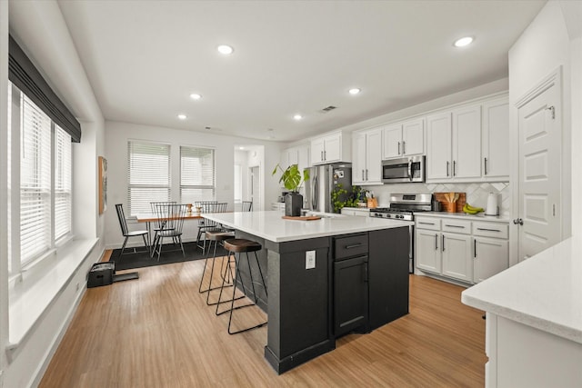 628 Claverton Ln, Forney, TX 75126 - kitchen with light wood-style floors, stainless steel appliances, light countertops, a kitchen bar, and white cabinetry