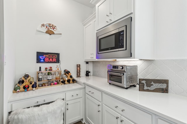 kitchen with a toaster, stainless steel microwave, tasteful backsplash, white cabinetry, and light countertops