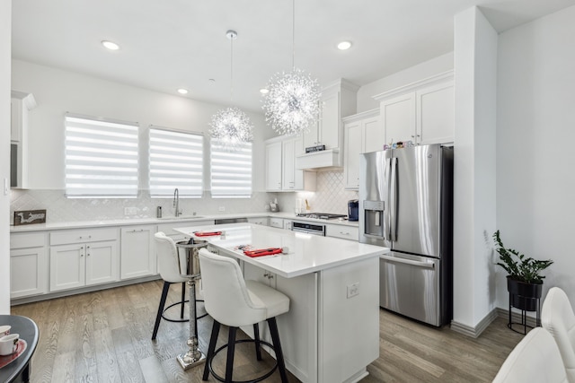 kitchen with a sink, tasteful backsplash, white cabinetry, light wood-style floors, and appliances with stainless steel finishes