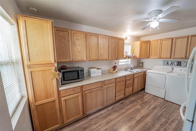 interior space featuring a sink, washing machine and dryer, a ceiling fan, wood finished floors, and laundry area