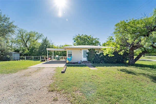 view of front of house featuring driveway, metal roof, fence, an outbuilding, and a front yard