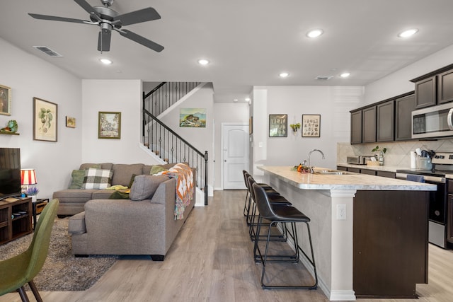 kitchen featuring a sink, light wood-style floors, stainless steel appliances, a center island with sink, and light countertops