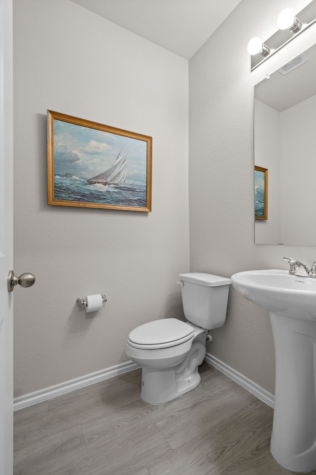 half bath featuring visible vents, wood finished floors, baseboards, and toilet