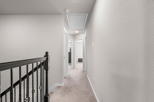 hallway with attic access, baseboards, an upstairs landing, and light colored carpet
