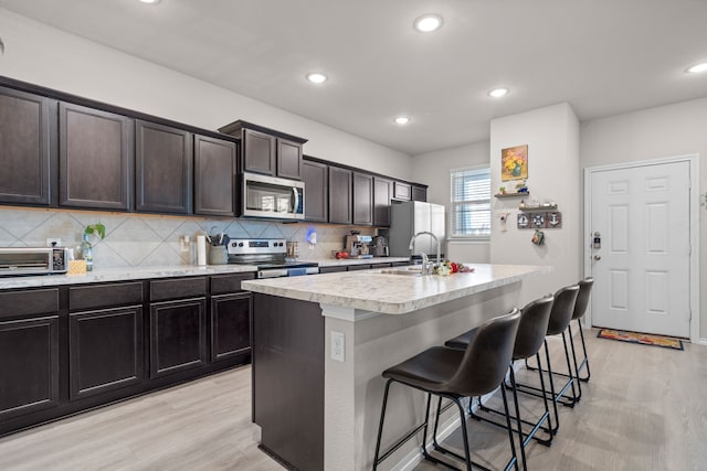 kitchen featuring tasteful backsplash, light wood-type flooring, light countertops, a breakfast bar, and appliances with stainless steel finishes