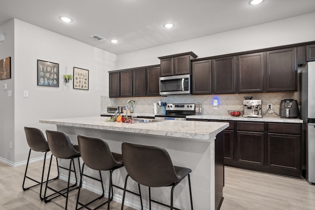 kitchen with stainless steel appliances, a kitchen breakfast bar, dark brown cabinets, visible vents, and light countertops