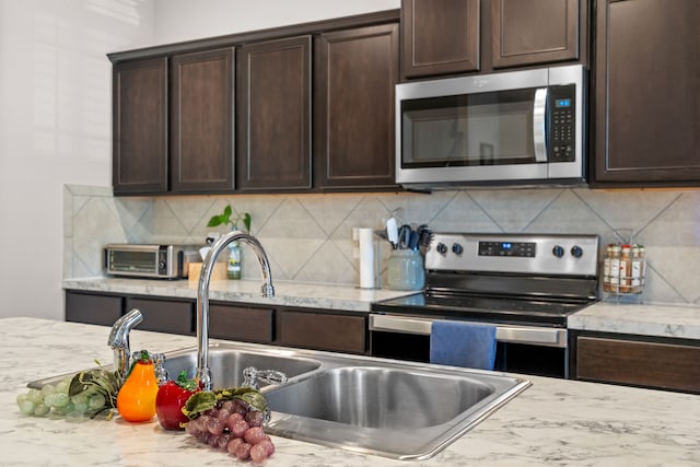 kitchen featuring dark brown cabinets, stainless steel appliances, and light stone counters