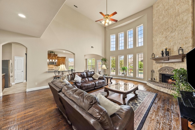 living area featuring ceiling fan, arched walkways, a brick fireplace, baseboards, and a high ceiling