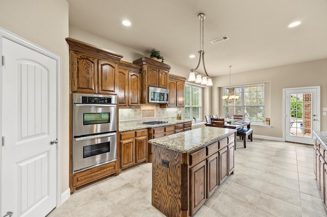 kitchen featuring visible vents, pendant lighting, light stone countertops, backsplash, and stainless steel appliances