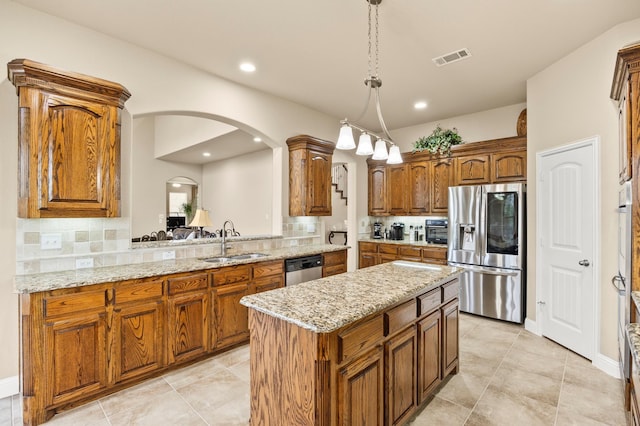 kitchen featuring a kitchen island, brown cabinets, a sink, backsplash, and stainless steel appliances