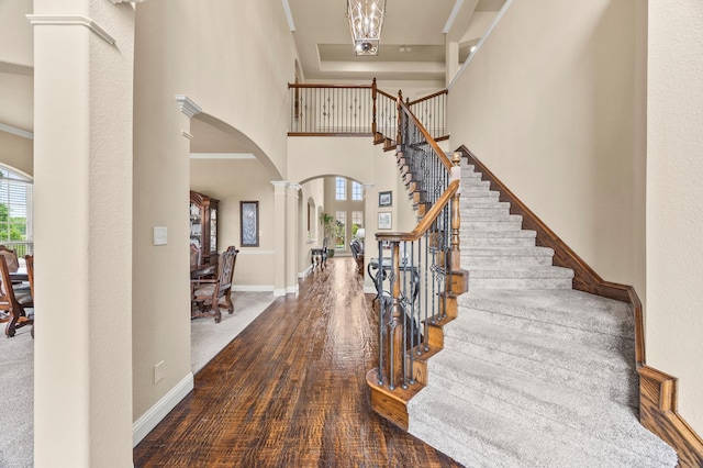 foyer featuring arched walkways, stairway, an inviting chandelier, a high ceiling, and ornate columns