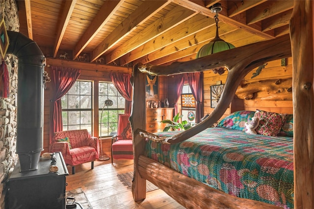 bedroom with wooden walls, a wood stove, wood-type flooring, beamed ceiling, and wood ceiling
