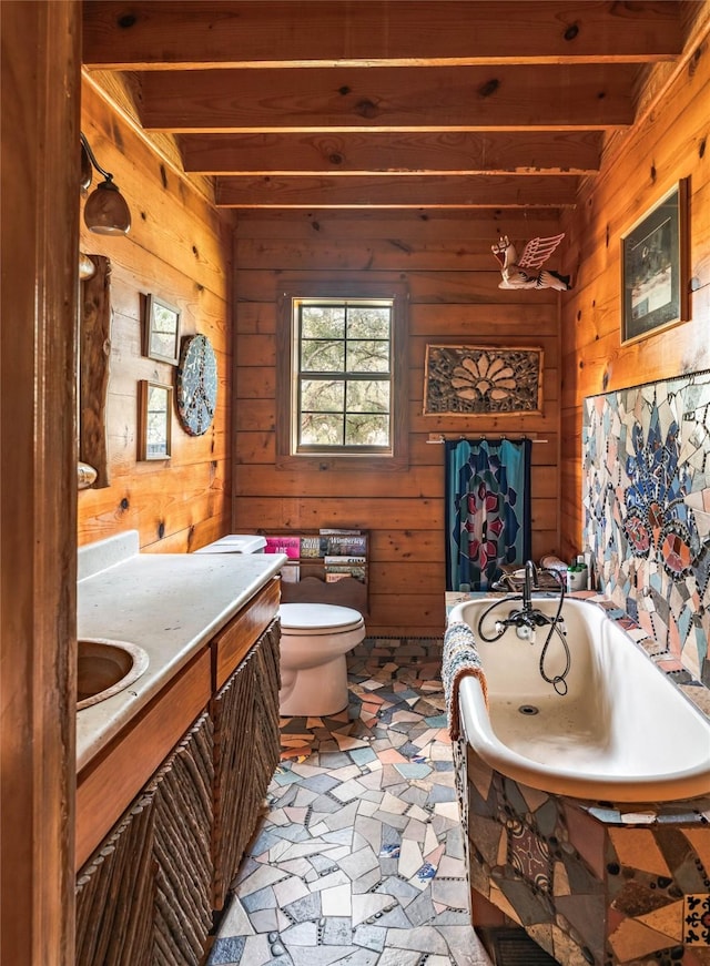 bathroom with wood walls, toilet, vanity, beamed ceiling, and a bath