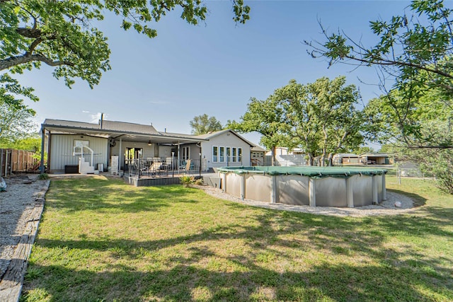 rear view of house with a lawn, a covered pool, fence, and ceiling fan
