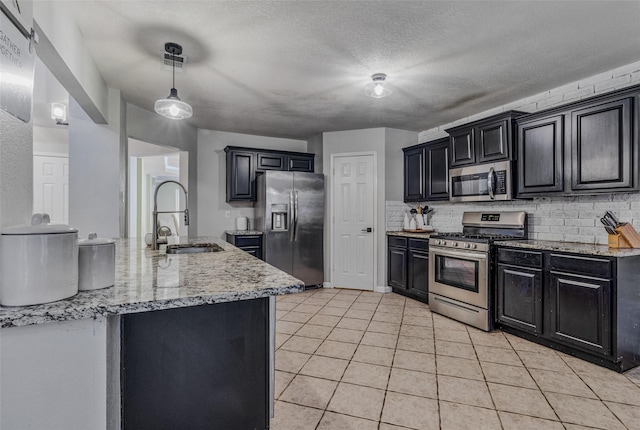 139 Wembley Way, Rockwall, TX 75032 - kitchen with dark cabinetry, stainless steel appliances, a sink, and light tile patterned floors