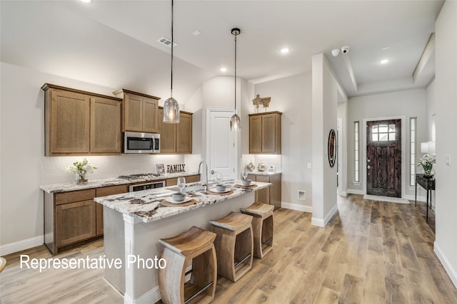 kitchen featuring stainless steel microwave, tasteful backsplash, light wood-style floors, light stone counters, and brown cabinetry