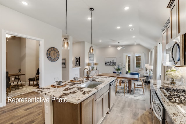 kitchen with light stone counters, stainless steel appliances, a ceiling fan, a sink, and light wood-style floors