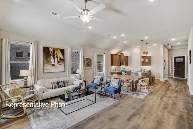 living area featuring vaulted ceiling, light wood-style floors, ceiling fan, baseboards, and visible vents