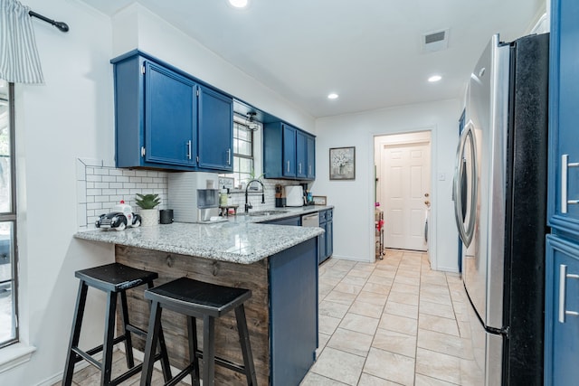 kitchen featuring tasteful backsplash, a sink, blue cabinetry, a peninsula, and appliances with stainless steel finishes
