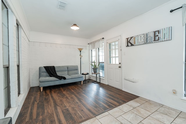 foyer entrance with brick wall, crown molding, wood finished floors, and visible vents