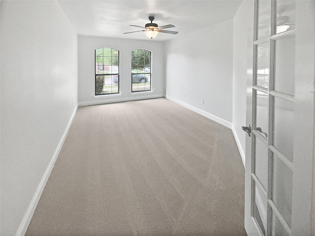 carpeted spare room featuring a ceiling fan, baseboards, and french doors