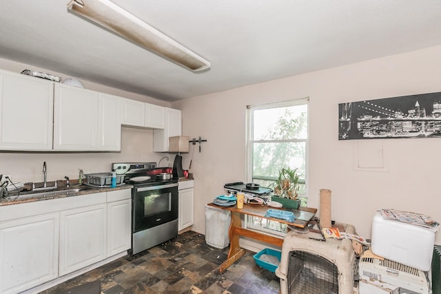 kitchen featuring stone finish flooring, stainless steel electric range, white cabinetry, and a sink