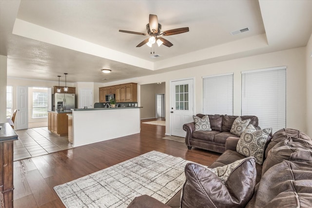 living area featuring a tray ceiling, visible vents, a ceiling fan, and dark wood-style flooring