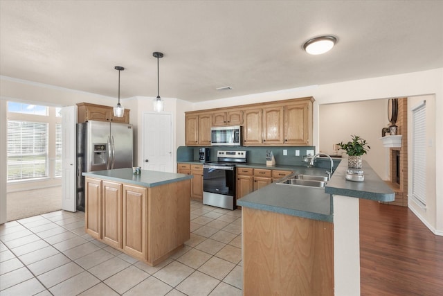 kitchen featuring stainless steel appliances, a center island, a peninsula, a sink, and a brick fireplace