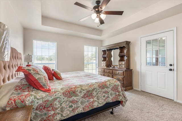 bedroom with ceiling fan, light carpet, a tray ceiling, and baseboards