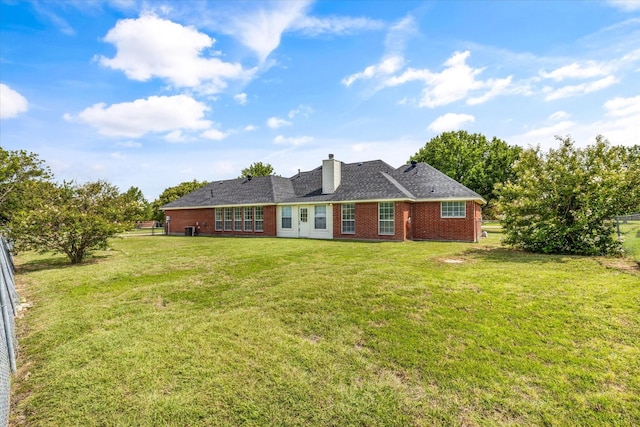 rear view of house with brick siding, a lawn, a chimney, and fence