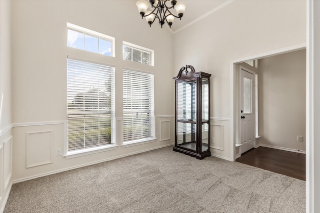 unfurnished room featuring a towering ceiling, ornamental molding, carpet floors, wainscoting, and a chandelier