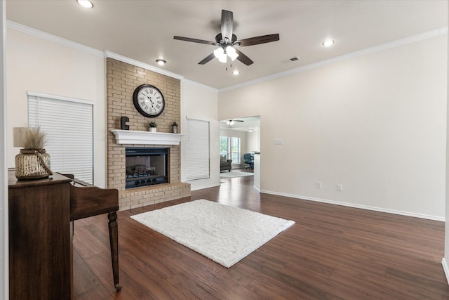 living area with dark wood-style flooring, visible vents, a brick fireplace, ceiling fan, and ornamental molding