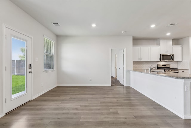 kitchen featuring decorative backsplash, stainless steel appliances, white cabinets, light stone countertops, and visible vents
