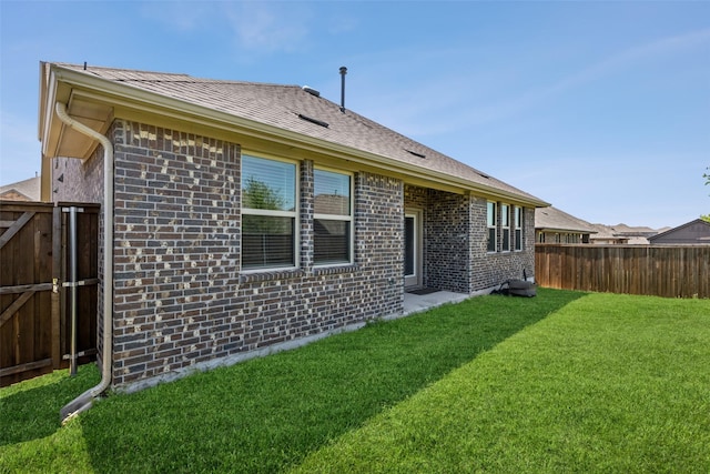 rear view of property featuring brick siding, a lawn, a fenced backyard, and a gate