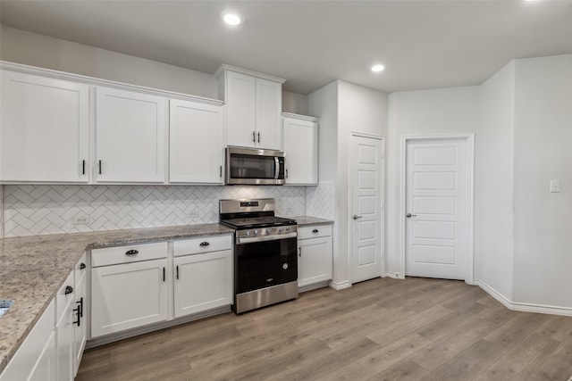 kitchen with white cabinets, light wood-style floors, stainless steel appliances, backsplash, and light stone countertops