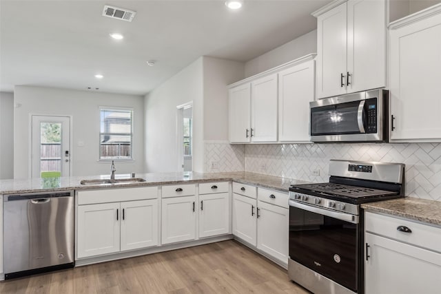 kitchen with light stone counters, a sink, appliances with stainless steel finishes, white cabinetry, and visible vents