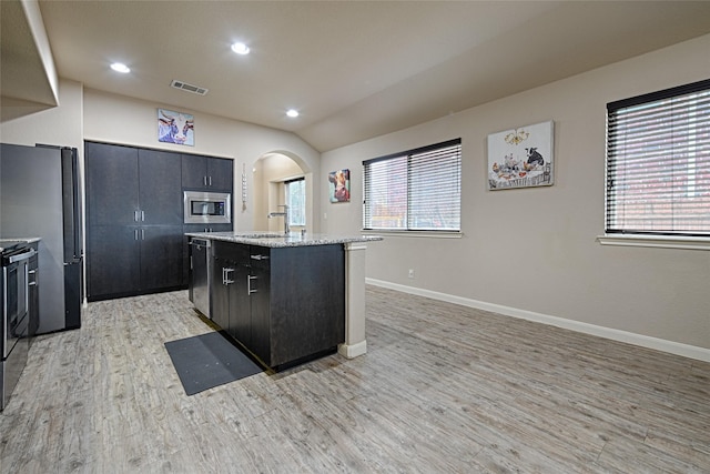 kitchen featuring a center island, light wood-type flooring, arched walkways, baseboards, and appliances with stainless steel finishes