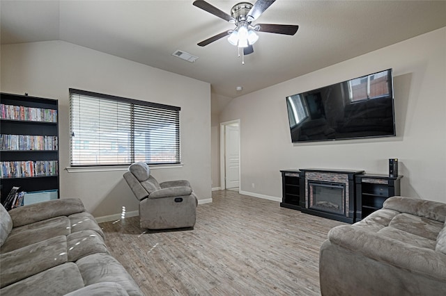 living area featuring lofted ceiling, wood finished floors, visible vents, a ceiling fan, and a glass covered fireplace