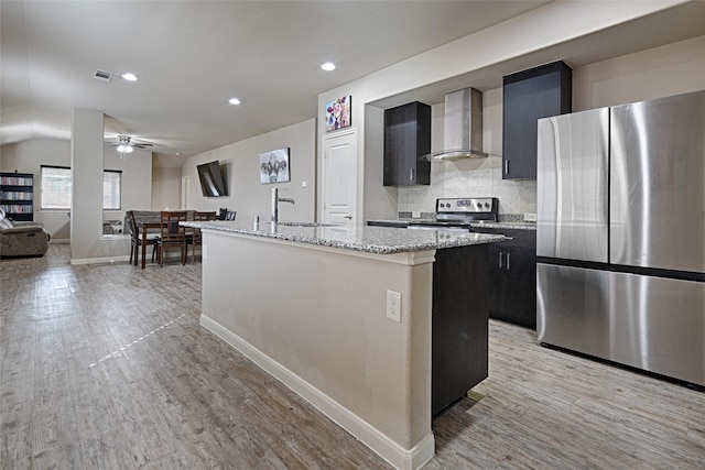 kitchen featuring stainless steel appliances, a ceiling fan, a sink, light wood-type flooring, and wall chimney exhaust hood