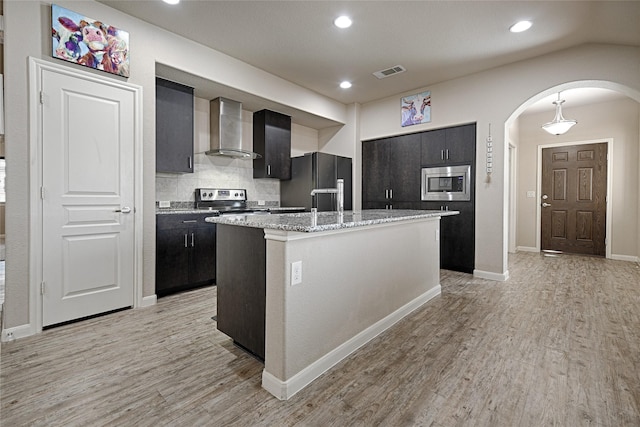 kitchen with arched walkways, light wood-type flooring, visible vents, wall chimney range hood, and appliances with stainless steel finishes